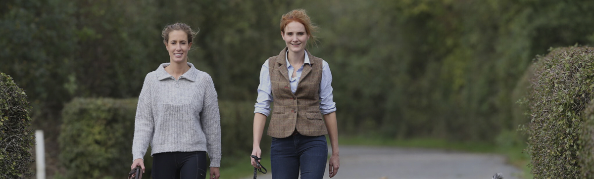 Das Übersichtsbild zu unseren Kursen. Man sieht im Hintergrund ein paar Menschen im Wald stehen. im Vordergrund liegen drei entspannte Hunde und warten auf den Rückruf.